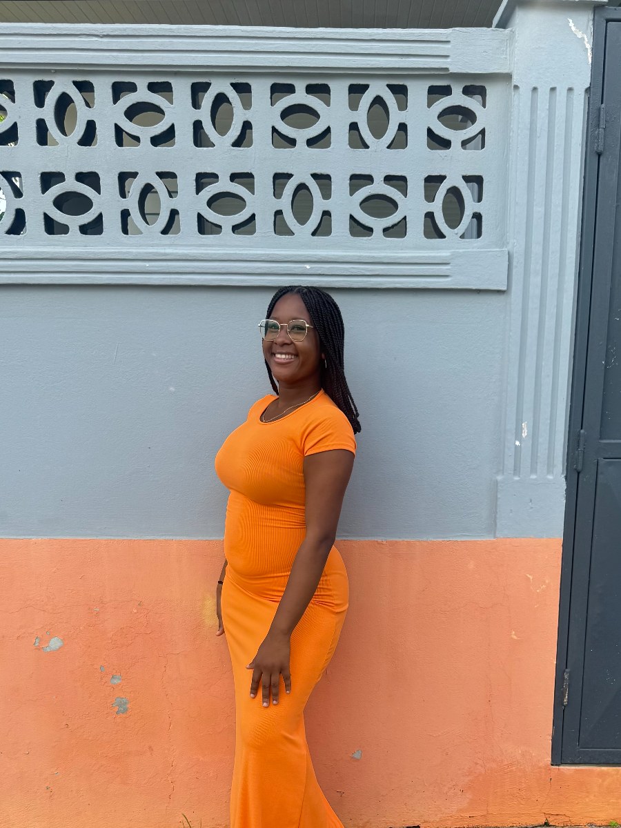 Géralda en robe orange devant un mur coloré